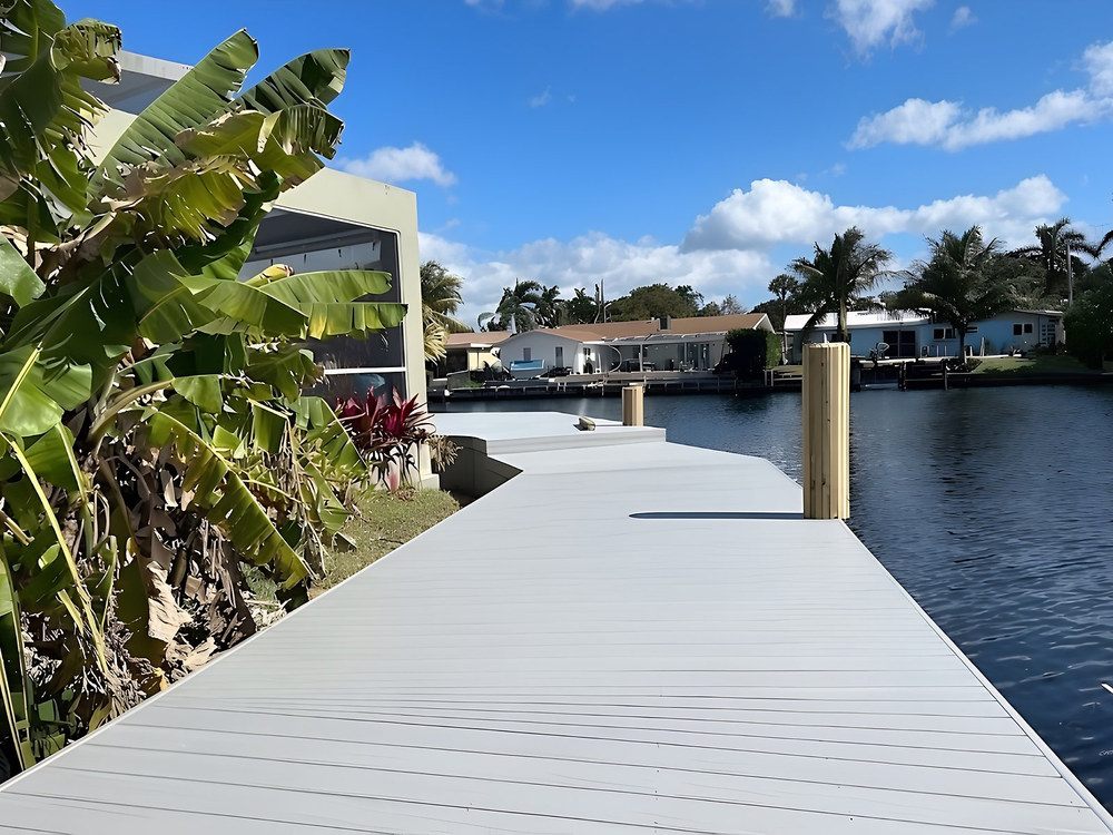 Grey composite dock curving along South Florida canal with tropical plants