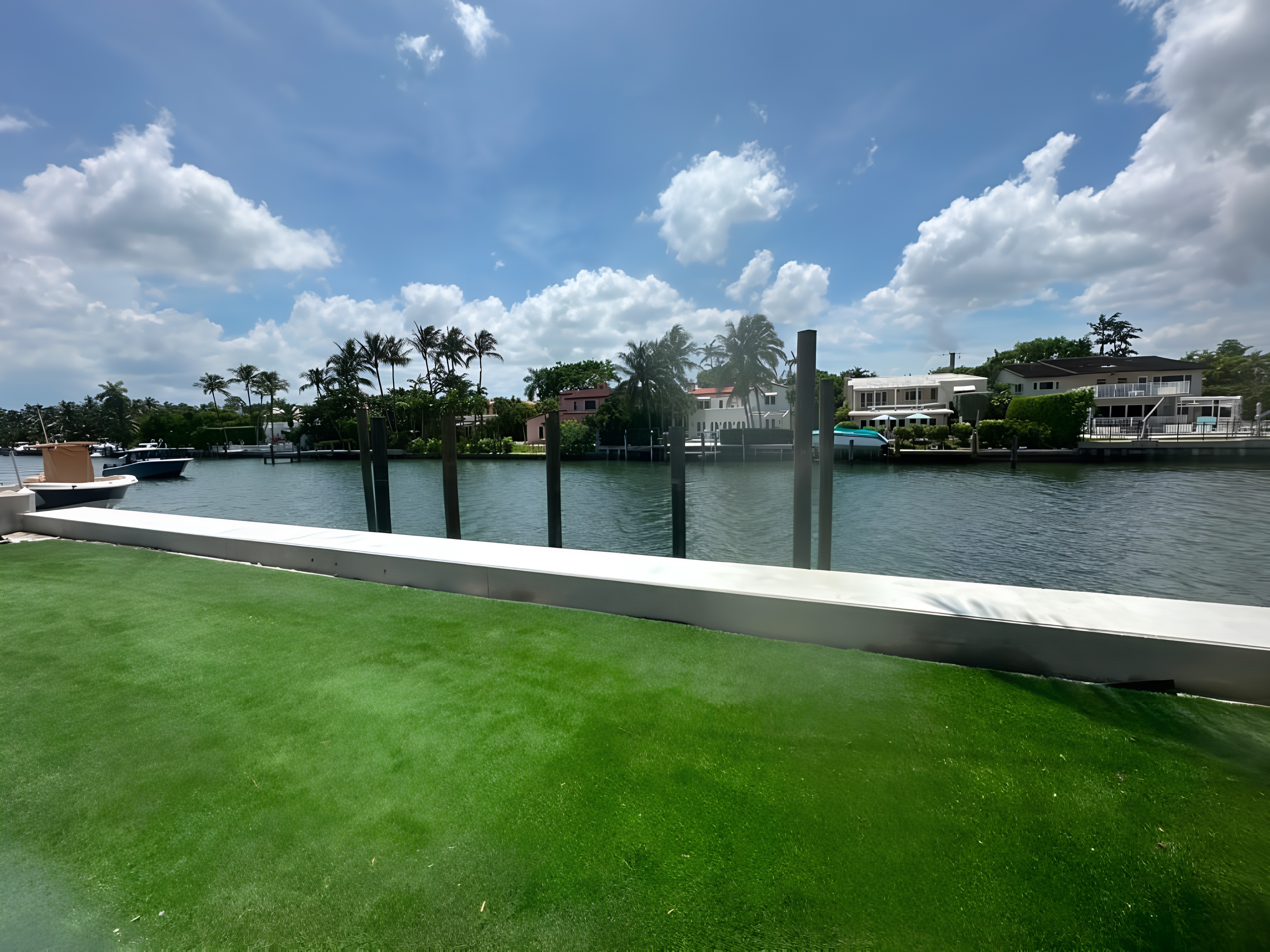 Completed seawall — lush green lawn, white concrete cap, pilings along sparkling South Florida canal — Contour Marine